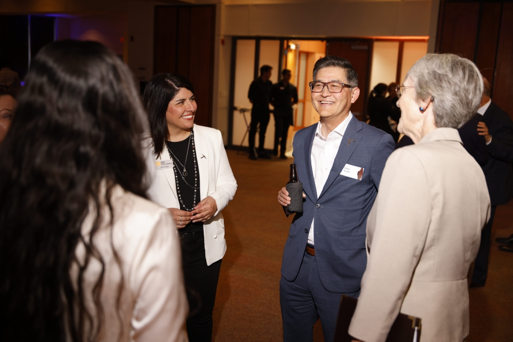 A man and two women smile while speaking together at the event.